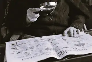 een hand die een vergrootglas beet houd boven een krant en stamboomonderzoek doet